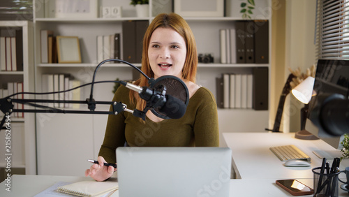 Принти на полотні Young female podcaster speaking into a microphone while recording at home
