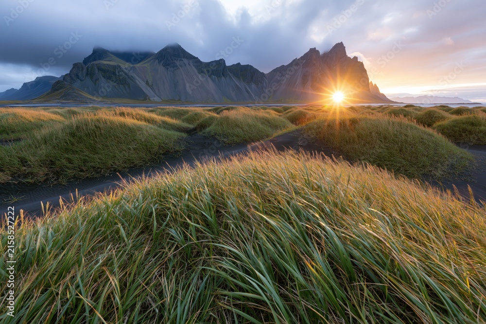 Naklejka premium The Sunrise Over Jagged Mountains and Grassy Dunes at Dawn