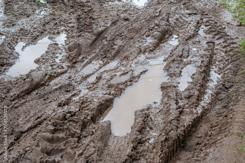 Autumn бездорожье in the countryside. On the muddy clay road, you can see traces of off‑road vehicles. There are no paved roads. After heavy rainfall, there are puddles on the rural road.