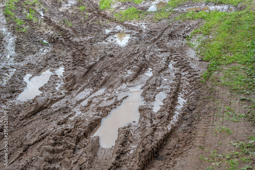 Autumn бездорожье in the countryside. On the muddy clay road, you can see traces of off‑road vehicles. There are no paved roads. After heavy rainfall, there are puddles on the rural road.