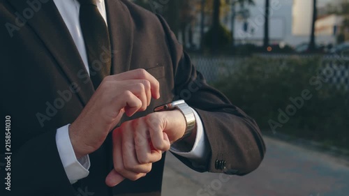 Businessman raises hand and looks at the smartwatch on it. Businessman is typing message on the smartwatch.  Modern gadgets and people concept. Modern communication. Close up, slow motion footage.