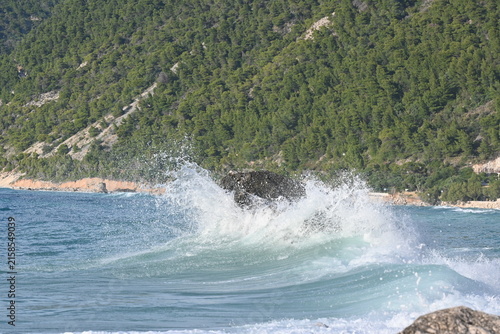Canvastavla Powerful turquoise ocean wave crashing with wide foam splash on a big rock, beau