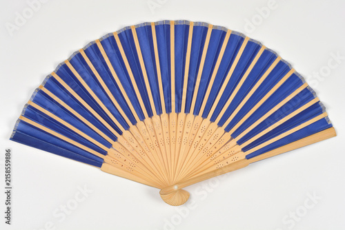 Fotografie Top view of an open oriental folding hand fan with light wood bamboo ribs and dark blue fabric centered on a white background