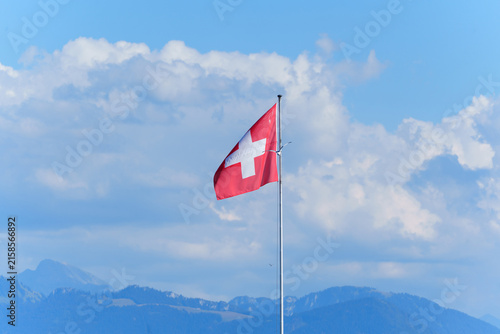 Swiss Flag Waving Proudly Against Blue Sky and Mountains in Morges