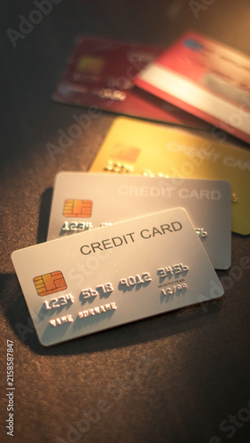 Multiple credit cards stacked on dark surface with spotlight on front silver card for payment options.