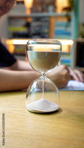Study and focus, sand flowing through glass hourglass on desk during work session