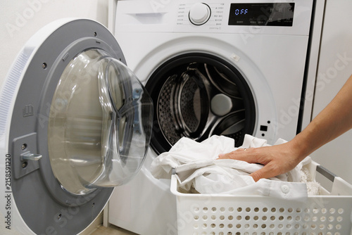 Naklejka Laundry basket full of washed clothes beside a washing machine. Simple home cleaning routine with fresh clothes ready for drying after laundry.