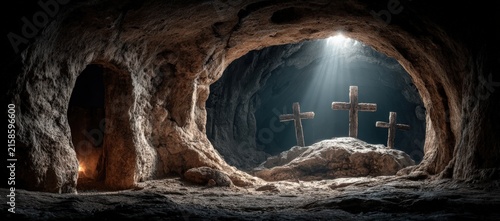Cave interior with three wooden crosses illuminated by light beams, rocky walls and a small opening visible in the background, creating a dramatic atmosphere