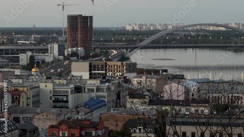 Kyiv cityscape at dusk with the Dnipro River, arched bridge, urban skyline and calm evening atmosphere. Panoramic view of modern architecture and historic riverside landscape.