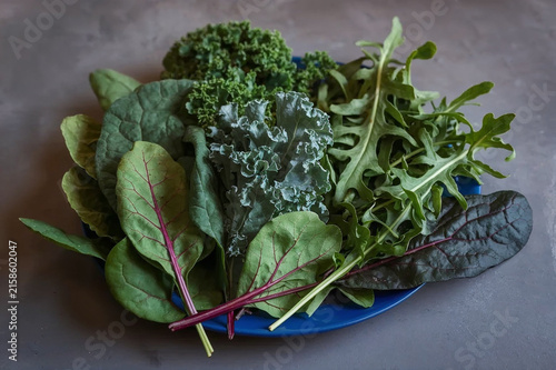 Obraz na płótnie Fresh assortment of leafy green vegetables including kale, arugula, lettuce and red-veined greens arranged on a blue plate, ideal for healthy food and nutrition concepts