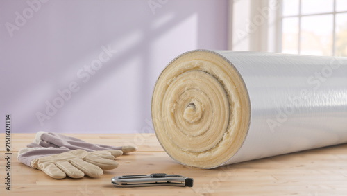Roll of thermal insulation material with work gloves and utility knife on a wooden table. Home renovation and energy efficiency concept. Copy space for text