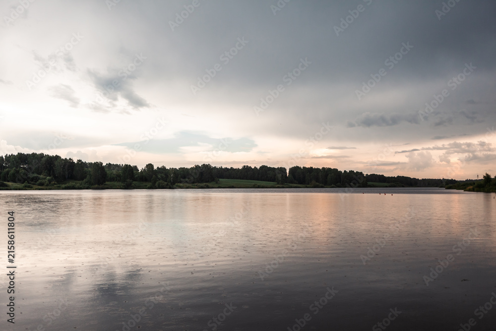 Fototapeta premium Tranquil view of a calm lake with reflections of cloudy skies and lush trees along the shoreline in a serene natural environment