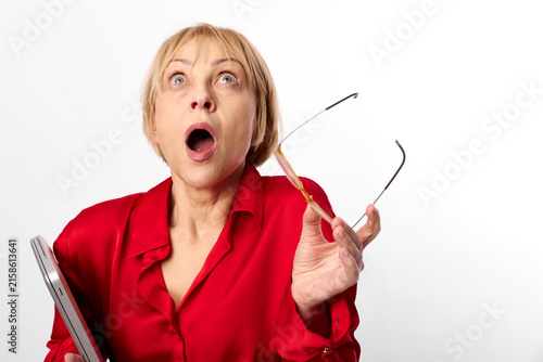 Surprised shocked woman in red blouse holding eyeglasses, portrait with wide open mouth, looking upward, studio white background, attentive startled expression closeup