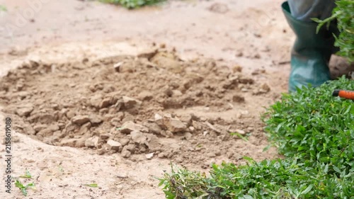 Digging the Earth: A close-up shot captures the action of digging in the earth, with soil being turned over and glimpses of green grass and boots indicating a gardening or landscaping activity.