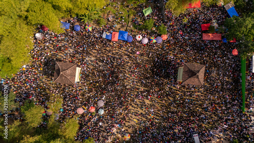 Aerial view of a massive crowd gathered in an open field with colorful umbrellas and two traditional structures in Klaten, Central Java, Indonesia.