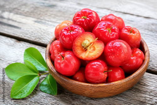 Fresh acerola cherries in wooden bowl with leaves on grey table, healthy fruit and natural food concept