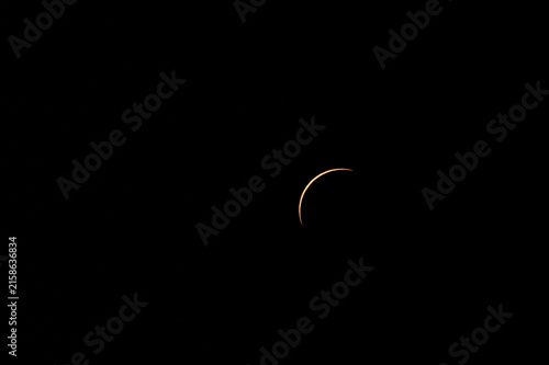 Telephoto view of a partial solar eclipse with the moon covering the solar disk, isolated against a dark sky background.