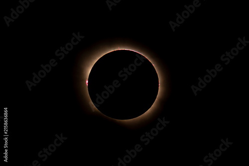 Telephoto astrophotography of total solar eclipse totality featuring a subtle solar corona and a vibrant pink solar prominence on the limb.