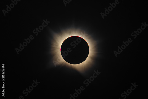 Telephoto view of total solar eclipse totality showing bright solar corona and red prominences isolated on dark space background