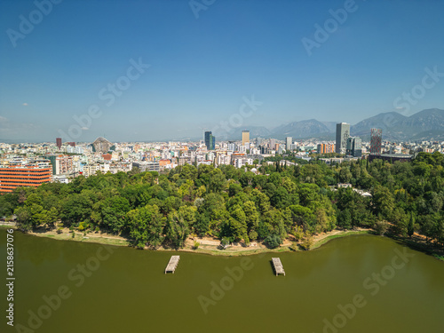 Fotografía Albania, Tirana 06 09 2025: Wide angle drone photo of Grand Park lake with two old concrete platforms in water, city skyline and mountains in background