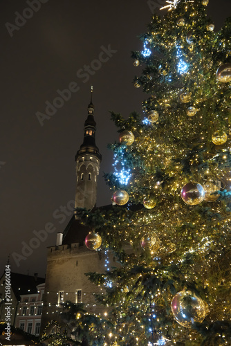 Low-angle of an illuminated Christmas tree with Tallinn Town Hall tower in the background at night