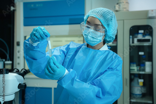 Team of medical laboratory technicians studying biotechnology sample with micro-scope and laptop for clinical trial.