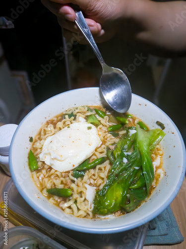 Obraz na płótnie Close-up of a hand holding a spoon over a hot bowl of spicy instant ramen noodle