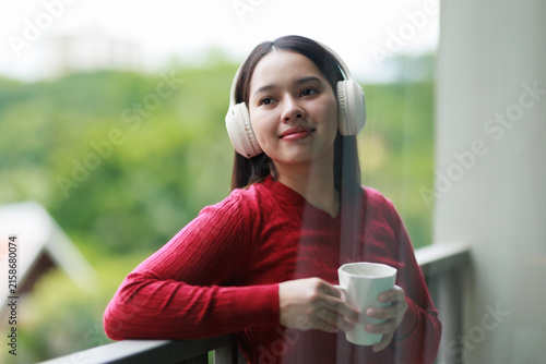 Bild auf Leinwand Young woman enjoying tranquil morning listening to music with headphones, holdin