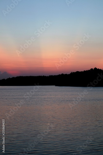 Photography Sunset crepuscular rays over a calm lake with tree line silhouette horizon verti
