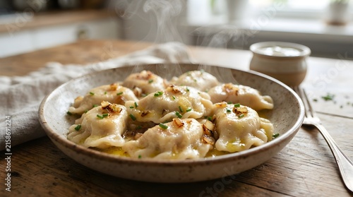 Plate of steaming hot pierogi topped with fried onions and chives on a wooden table