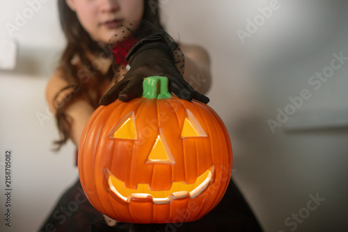 Girl is holding a Halloween pumpkin lantern towards the camera. selective focus