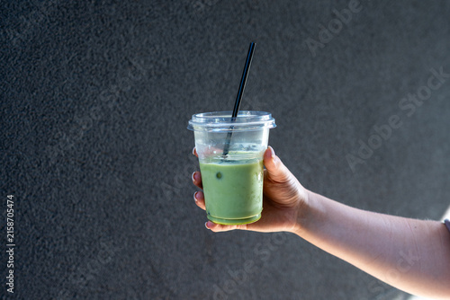 Konstfotografi Iced matcha green tea latte in takeaway plastic cup held by hand outdoors