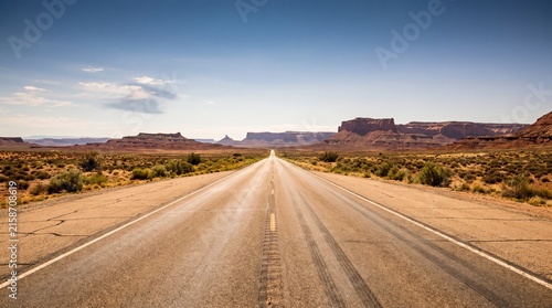Empty asphalt road stretching through a vast desert landscape towards distant mesas.