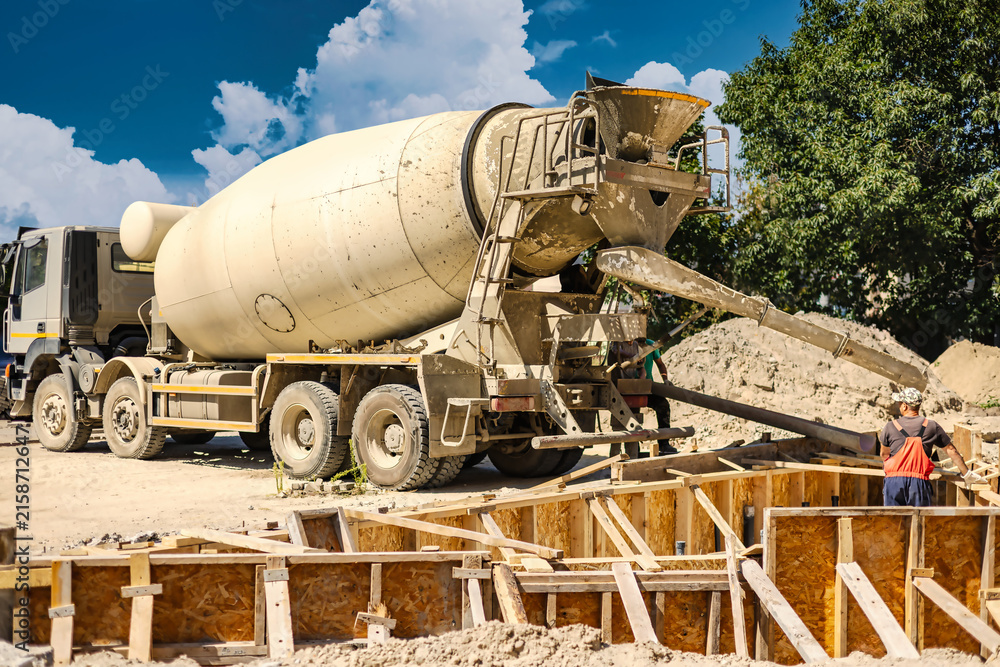 Naklejka premium Construction workers are operating a concrete mixer at a building site. They pour cement into wooden forms. Workers are busy with their tasks in the afternoon