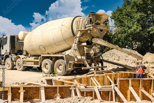 Construction workers are operating a concrete mixer at a building site. They pour cement into wooden forms. Workers are busy with their tasks in the afternoon