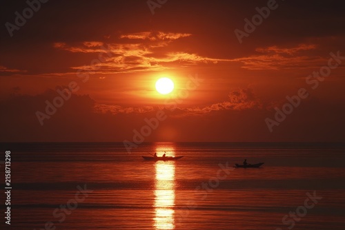 Fiery sunrise over calm ocean with fishing boats