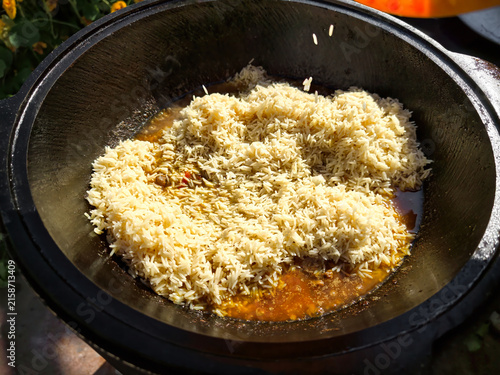 Foto Rice is being prepared in a kazan with meat and spices in an outdoor area surrounded by plants