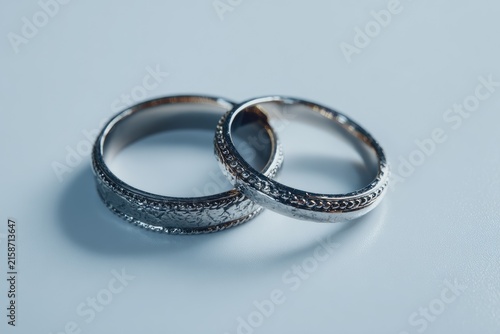 Two delicate, engraved wedding bands, light gray metal, rest atop a plain white surface