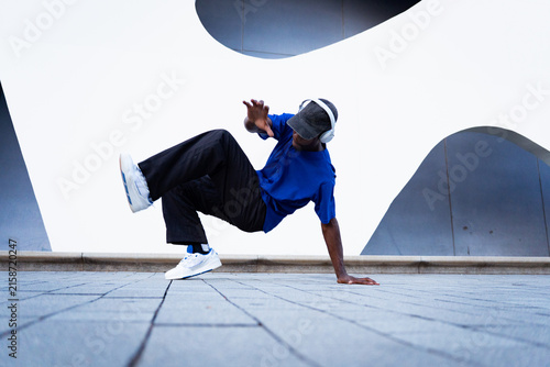 Quadro su tela Young black man performing a breakdance move on a paved urban floor, listening t