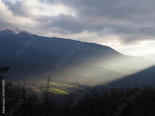 Fotografie Sunbeam hitting green hills through morning mist near Rigoso