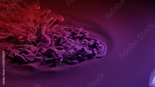 Abstract red and purple ink clouds swirling gracefully on a liquid surface with ripples.