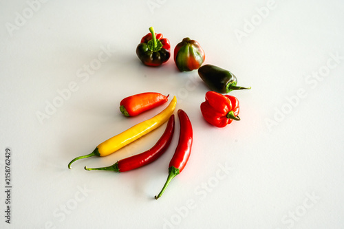 A vibrant variety of fresh chili and sweet peppers in red yellow orange and green arranged on a white background a colourful assortment of spicy vegetables rich in vitamin C.