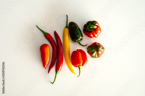 Bild auf Leinwand A colourful arrangement of fresh chili peppers jalapenos and sweet peppers in red yellow and green on a white background a vibrant variety of spicy vegetables from above