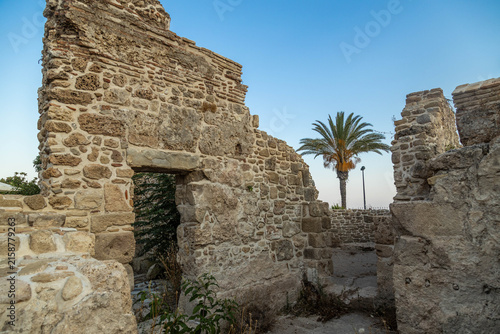 Obraz na plátně Ancient stone ruins with an archway against the background of a blue sky and green palm
