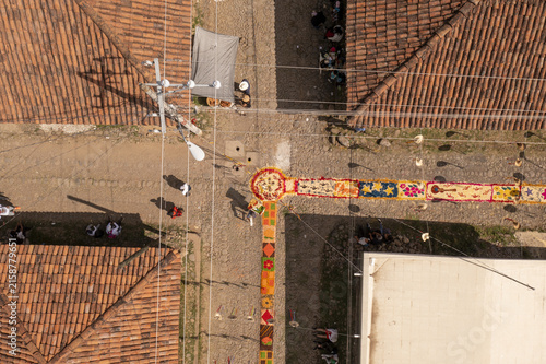 Aerial view of the intricate Patamban floral rug on a cobblestone street, surrounded by terracotta-tiled rooftops and people observing the colorful patterns in Patamban, Michoacan, Mexico.