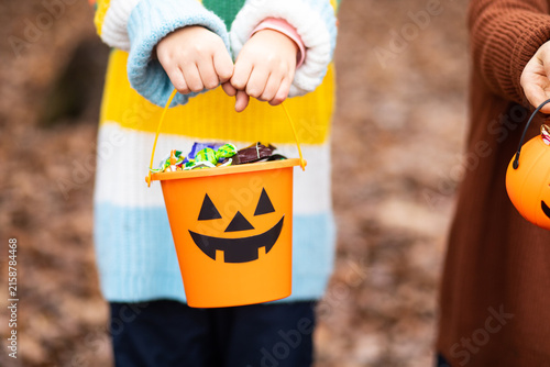 Kid child in a colorful striped sweater holds a Halloween pumpkin bucket filled with candy