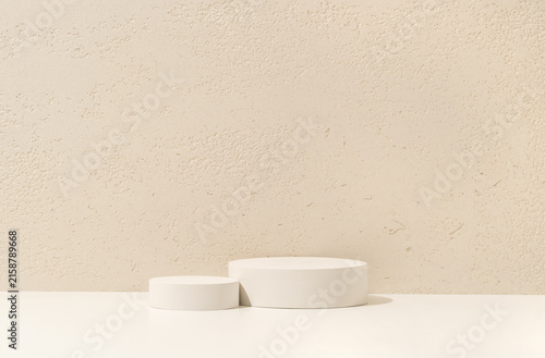 Two White Cylinder Podiums of Different Heights on White Shelf Against Travertine Wall Background