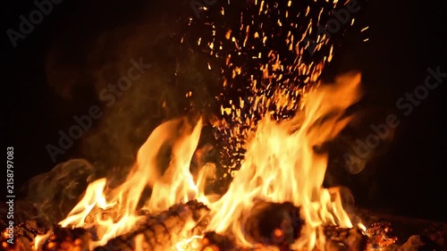 Close up of vibrant orange flames flickering on burning wood logs in a campfire at night with glowing sparks
