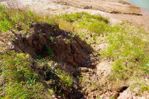 Bild auf Leinwand Deep soil erosion scars a grassy hillside, exposing raw earth and clay layers wh