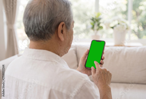 Elderly man holding smartphone with green screen mockup from behind